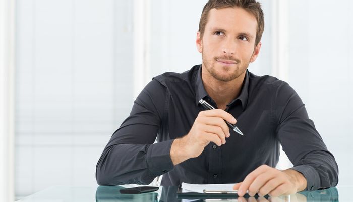 Entrepreneur sitting at a desk writing a document while thinking