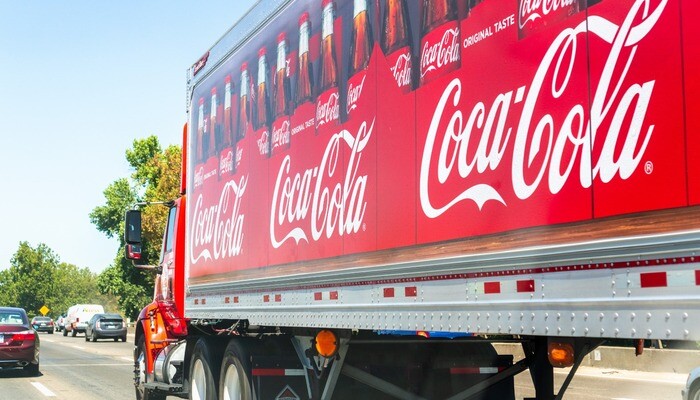 Coca Cola truck driving on the interstate; Coca Cola logo printed on the side